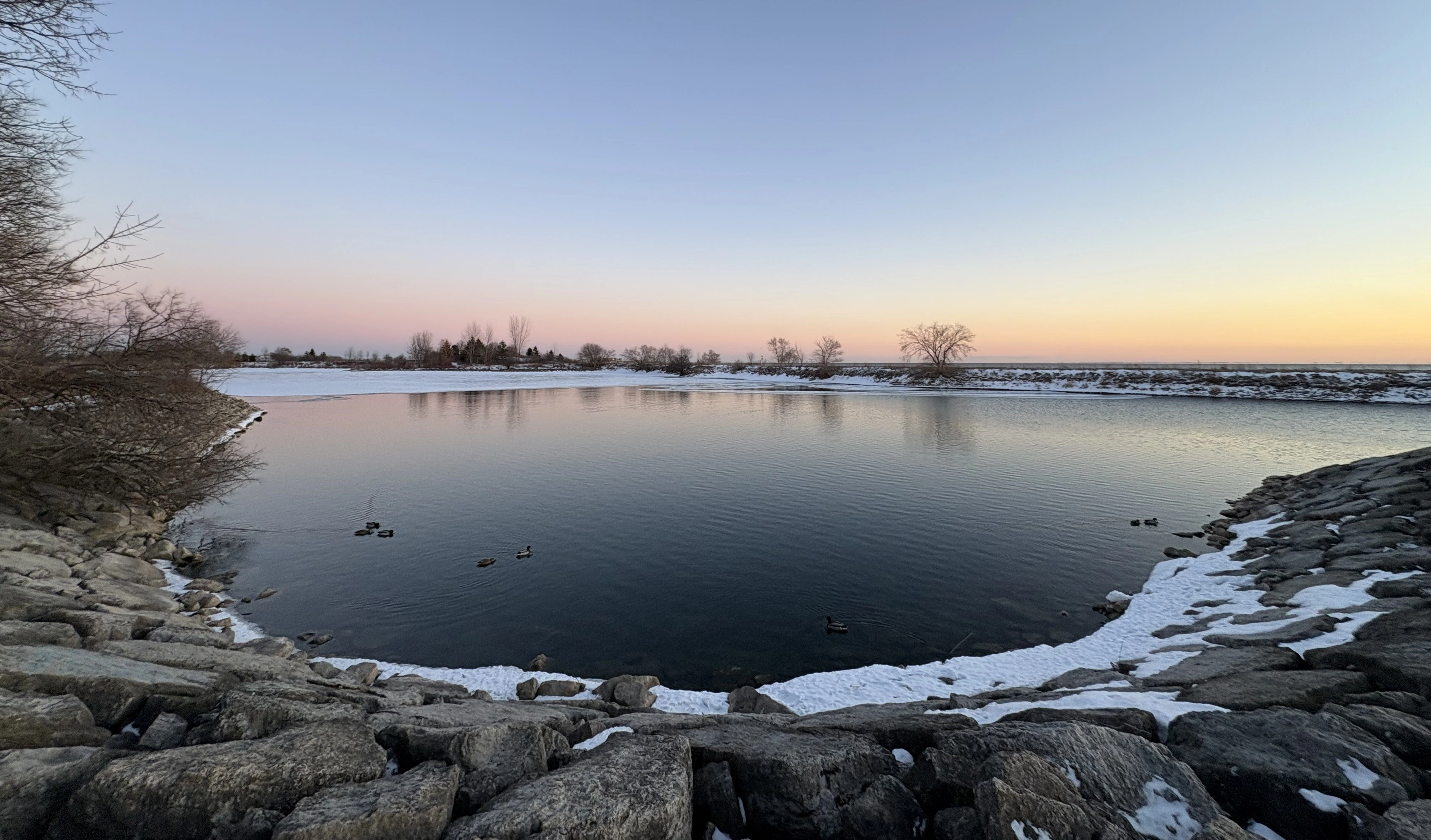 Ducks on a calm sheltered inlet at Colonel Samuel Smith Park at dusk in winter, with snow on the banks and a pastel sky